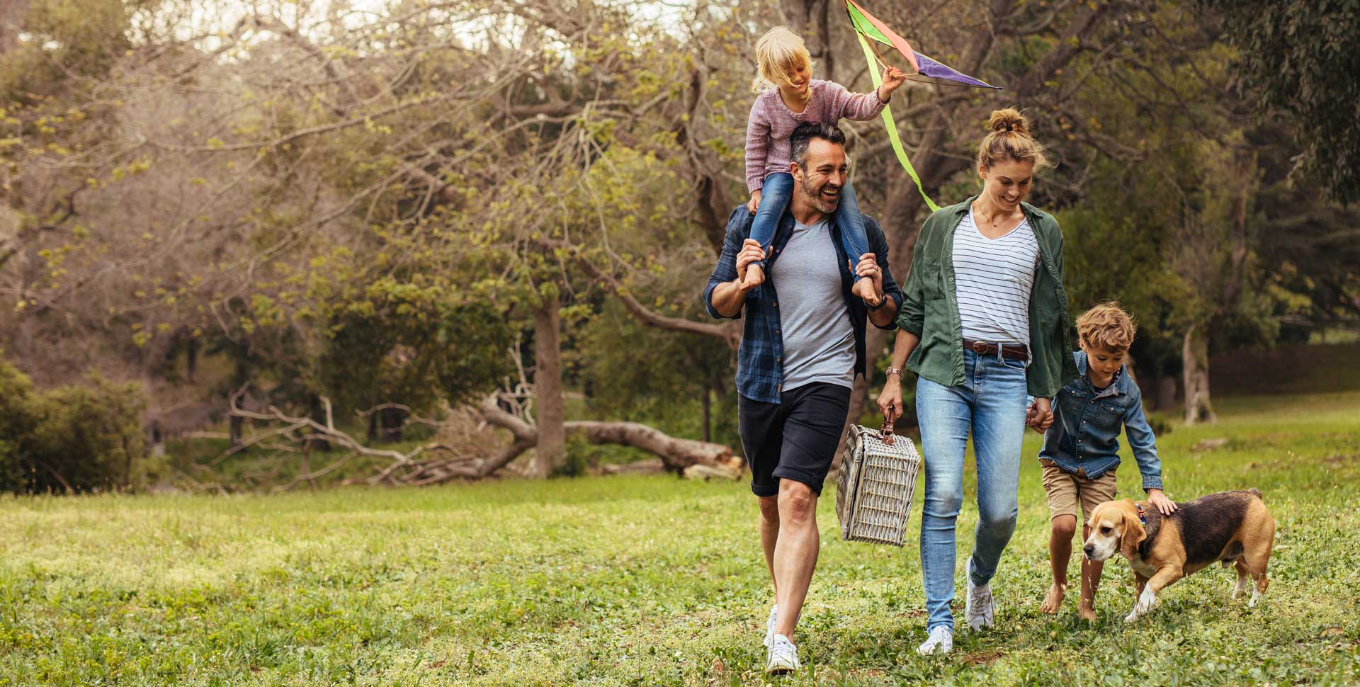 Family walking in meadow with dog and picnic basket